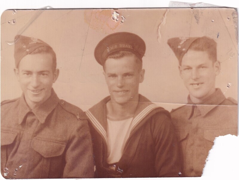 The image is an aged sepia-toned photograph showing three men in military uniforms, suggesting a historical context, possibly World War II. The man on the left and the man on the right wear similar uniforms with button-up jackets and berets, while the man in the center wears a naval uniform with a sailor's hat. The photograph is creased and has visible wear, including a torn lower right corner and spots of discoloration at the top.