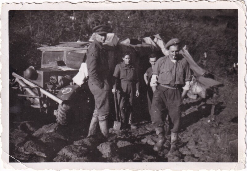 Soldiers standing beside a truck driving through the mud, front