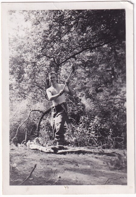 A photo of W.I. (Bill) Hann cutting branches from a tree with an ax taken in [East Anglia] England