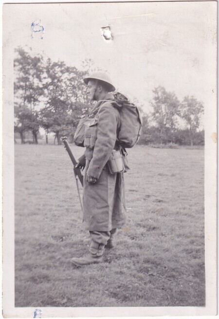 A photo of W.I. (Bill) Hann standing in a field wearing his army uniform in full kit viewed from the side taken in [East Anglia] England