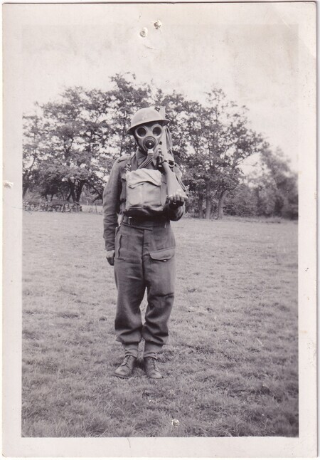 A photo of W.I. (Bill) Hann standing in a field wearing his army uniform with a gas mask taken in [East Anglia] England